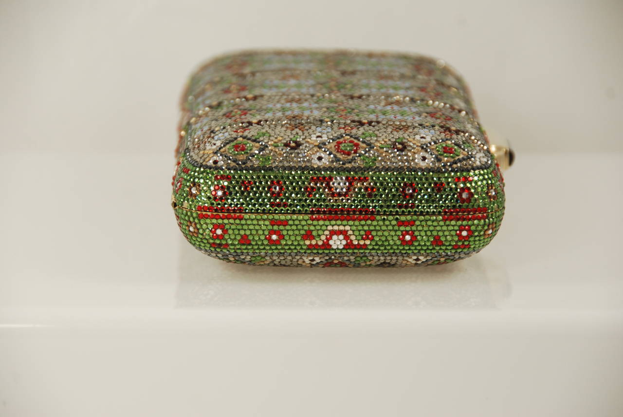 Exotic Judith Leiber minaudiere done in a tribal pattern to mimic a Persian Carpet. The background color is a silver-ish and there are rhinestones in the design in red, green, clear, and gold. The clasp is a black onyx, bag closes securely with an