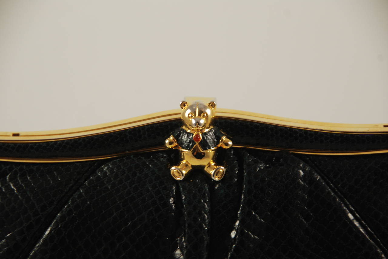 Judith Leiber black karung clutch with optional shoulder chain with a teddy bear clasp. The clasp lifts to open and works well. Bag closes securely. The optional shoulder chain folds into the bag when not in use. Inside is lined in balck facric and