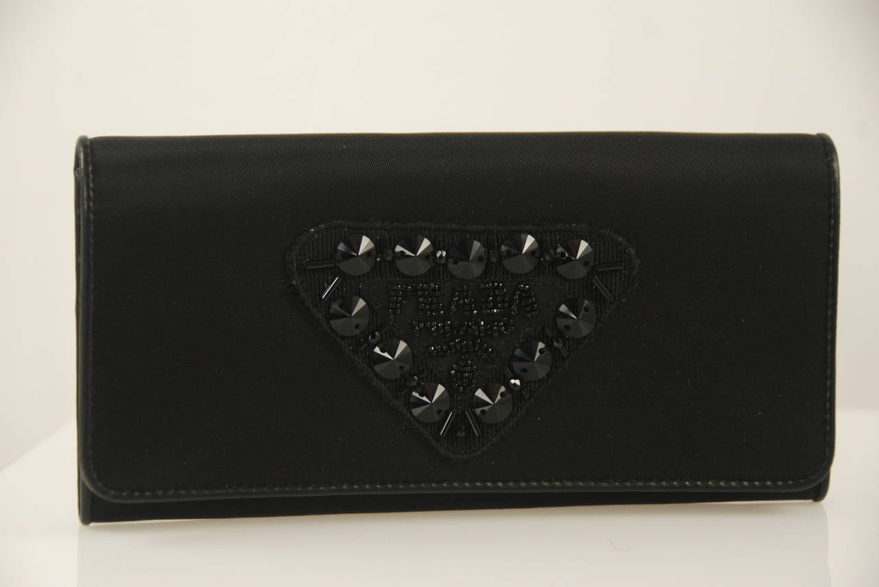 Black satin Prada evening wallet that is large enough to be used as a small evening bag. Inside is lined in black leather. There are numerous slots and compartments inside to keep you organized. There are rings on the inside to which you can attach