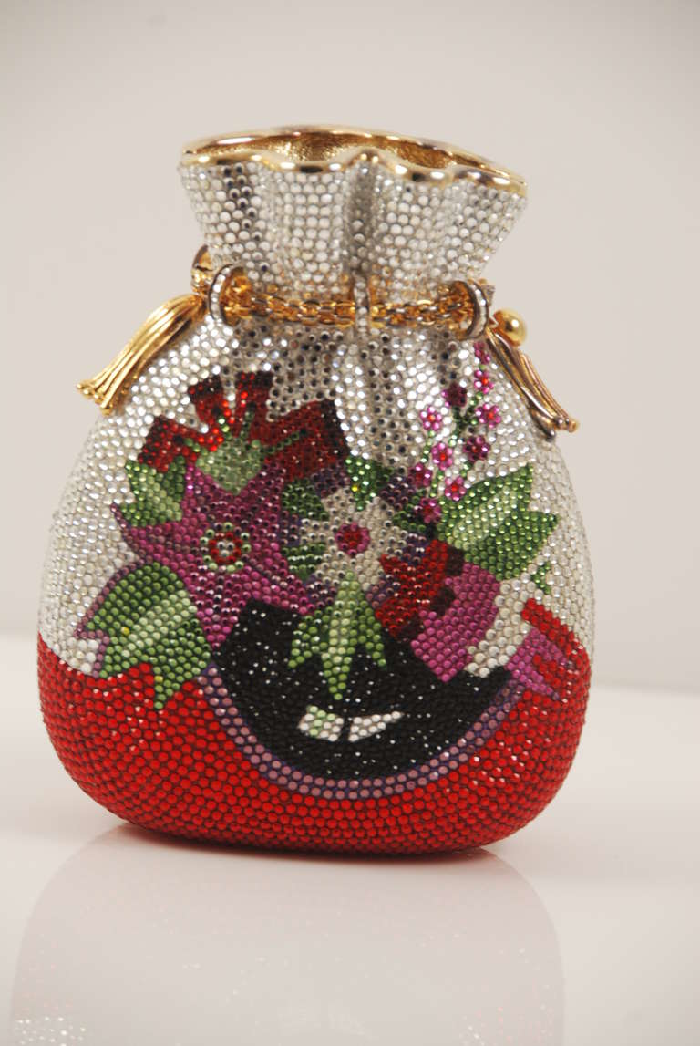 Colorful, jewel encrusted Judith Leiber minaudiere from the 1990s. The front and obverse have a bouquet of colorful flowers on a background of cleat rhinestones. There is an optional chain that folds into the purse when not in use and has a drop of