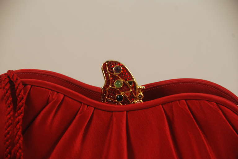 Judith Leiber red satin evening bag with jewel encrusted butterfly clasp and optional red cord shoulder strap. The strap folds into the bag when not in use so bag can be used as a clutch as well as a shoulder bag. The butterfly clasp is encrusted