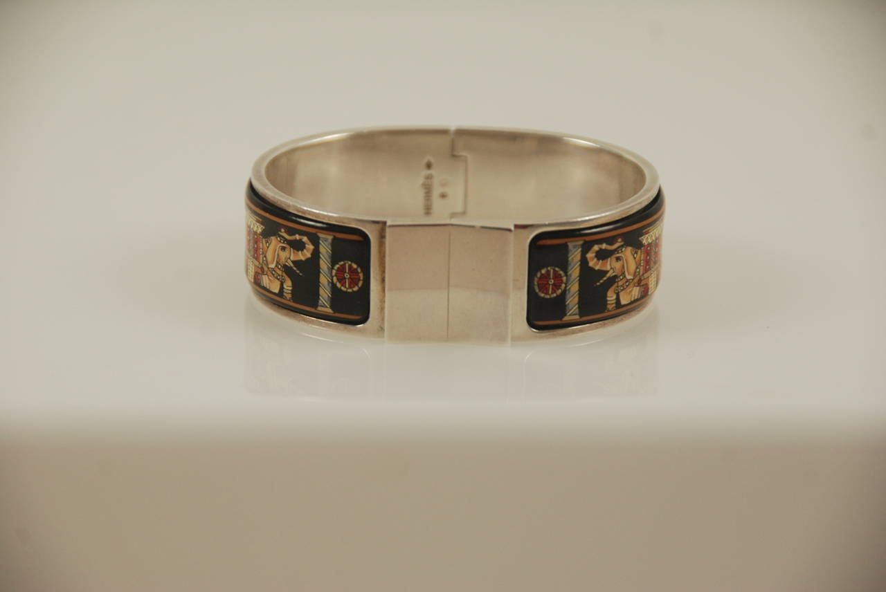 Hermes enamel bracelet with two plaques depicting elephants. The background is black, the elephants in gold  with red and orange details. The metal is palladium plated. To open the lock you push up on the lower right hand corner of the square. Lock