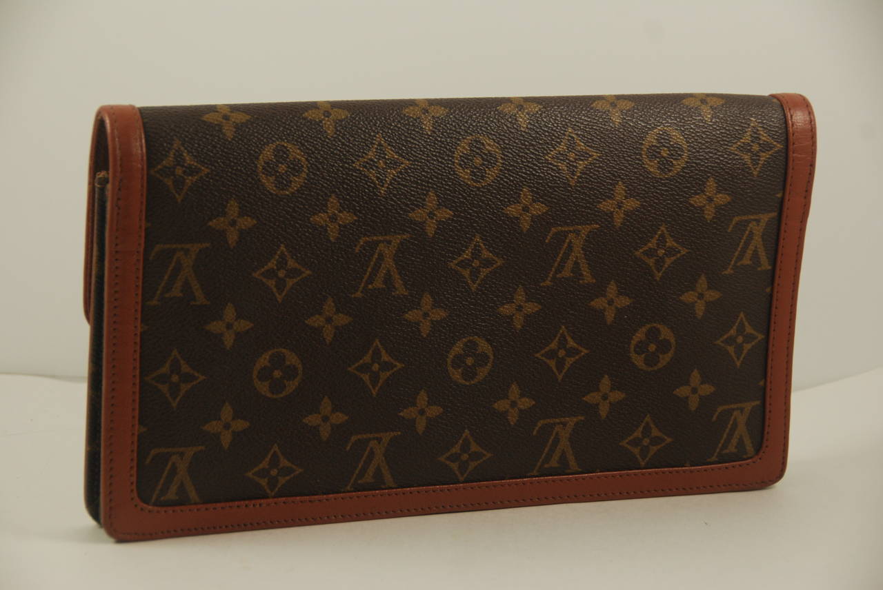 Louis Vuitton monogram canvas clutch from the late 1970s or early 1980s with leather trim. Inside lining is same color leather as the trim. There is one zipper side compartment and two slip compartments, one for lipstick and the other is large