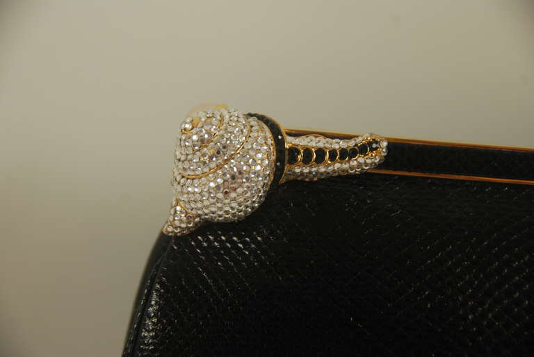 Judith Leiber black karung (lizard) clutch/shoulder bag with rhinestone snail clasp. Bag opens by pushing down on a pearl behind the snail. There is a black karung  strap that folds into the bag when not in use. The strap has an approx. 19