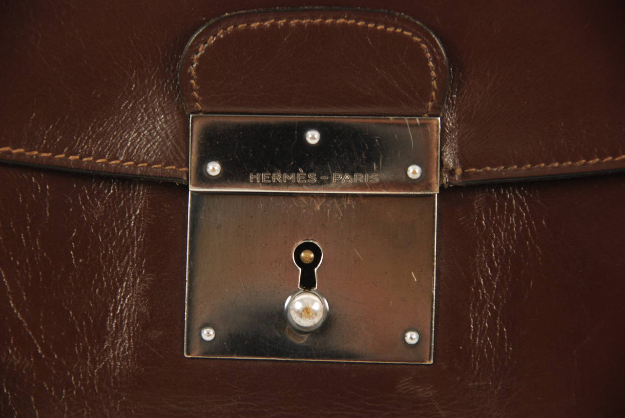 Vintage Hermes brown smooth leather portfolio from circa 1960s - 70s. The front plate and lock have a gun metal color finish. Comes with the  keys. Inside is lined with similar leather. Has a wrist strap that measures  approx. 13.5