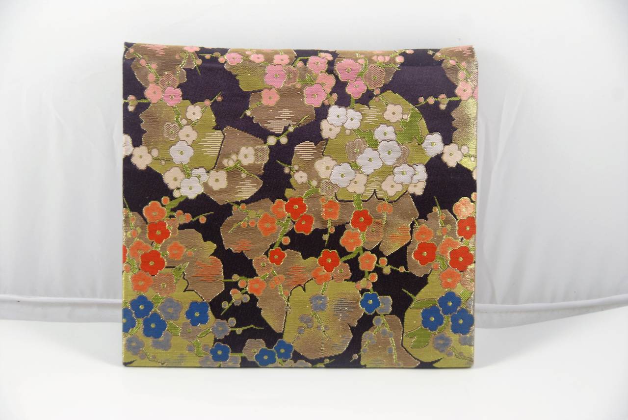 Diane Love evening bag from the 1970s done in a brocade fabric that is reminiscent of a Japanese fabric. The background color is deep purple. There is shimmery gold against the purple with small flowers of light and dark burnt orange, slate blue,