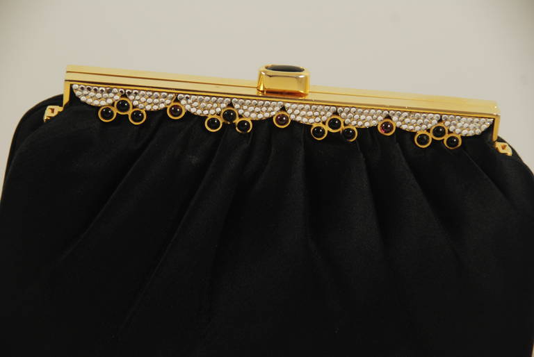 Elegant Judith Leiber black satin evening bag from 1986 with frame embellished in clear rhinestones, onyx and cabochon garnets. The clasp is onyx. The frame decorations are on both sides of the bag. The bag can be used as a clutch or a shoulder bag.