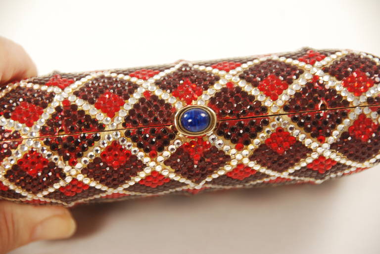 Judith Leiber minaudiere done in an interesting pattern. Inside each clearbox are two shades of red rhinestones. It is a sort of an op art pattern. All rhinestones are present and clear and sparkle. THe clasp is lapis. Clasp works well and bag