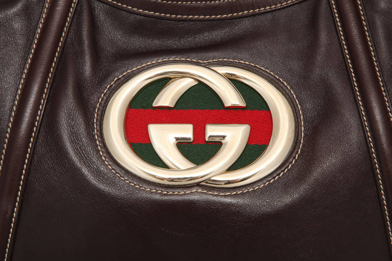 Gucci brown leather shoulder bag with large intertwined Gs on top of the classic red and green Gucci canvas ribbon. Inside is lined in brown fabric. There is one zipper compartment and one pocket that would hold a cell phone or a a small smart