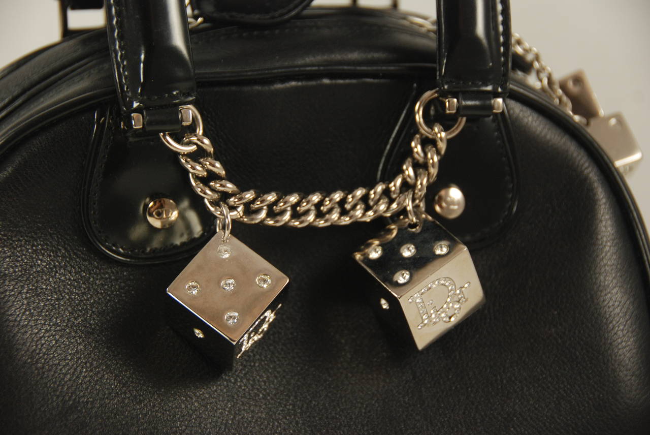 Fun and sassy Dior bag, in a bowling bag style shape. The body of the bag is black pebble grain leather and the handles and pipping are polished black leather. The dice charms are large and shiny and have rhinestones for the dots and the 