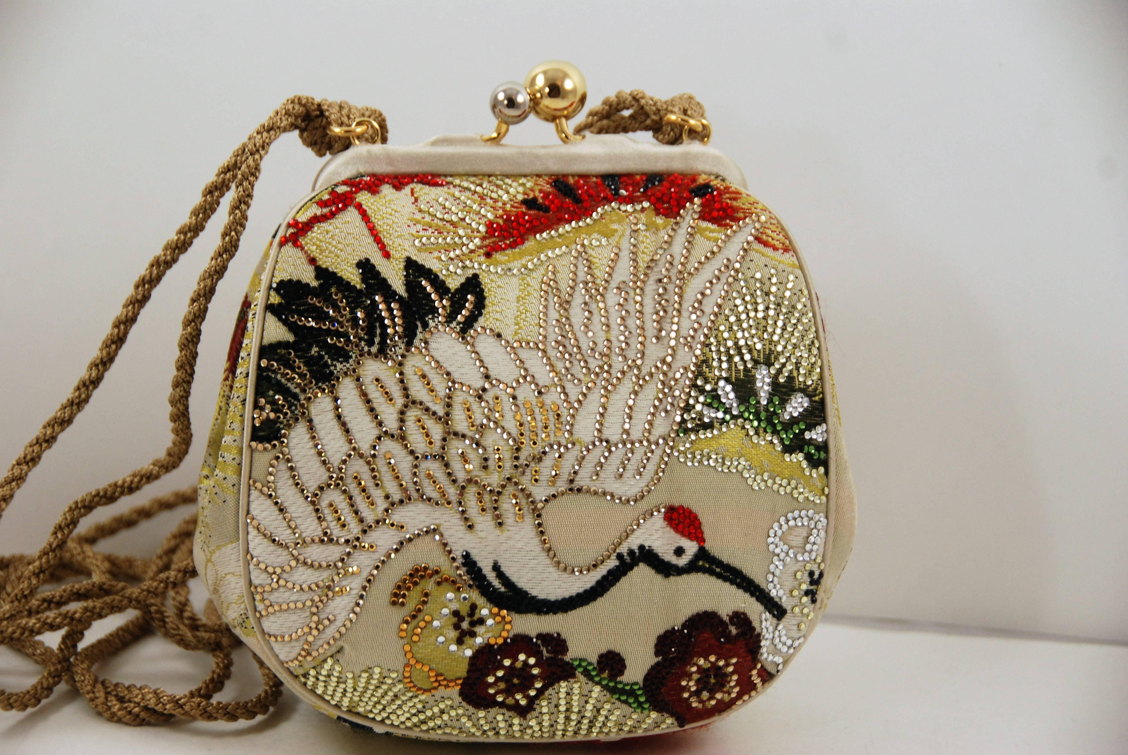 Judith Leiber obi bag fashioned out of A Japanese obi sash. Obi bags are among the most collectible Leiber bags. The bag features an elegant crane motif outlined in gold, black, and red crystals surrounded by an embroidered floral motif. The kiss
