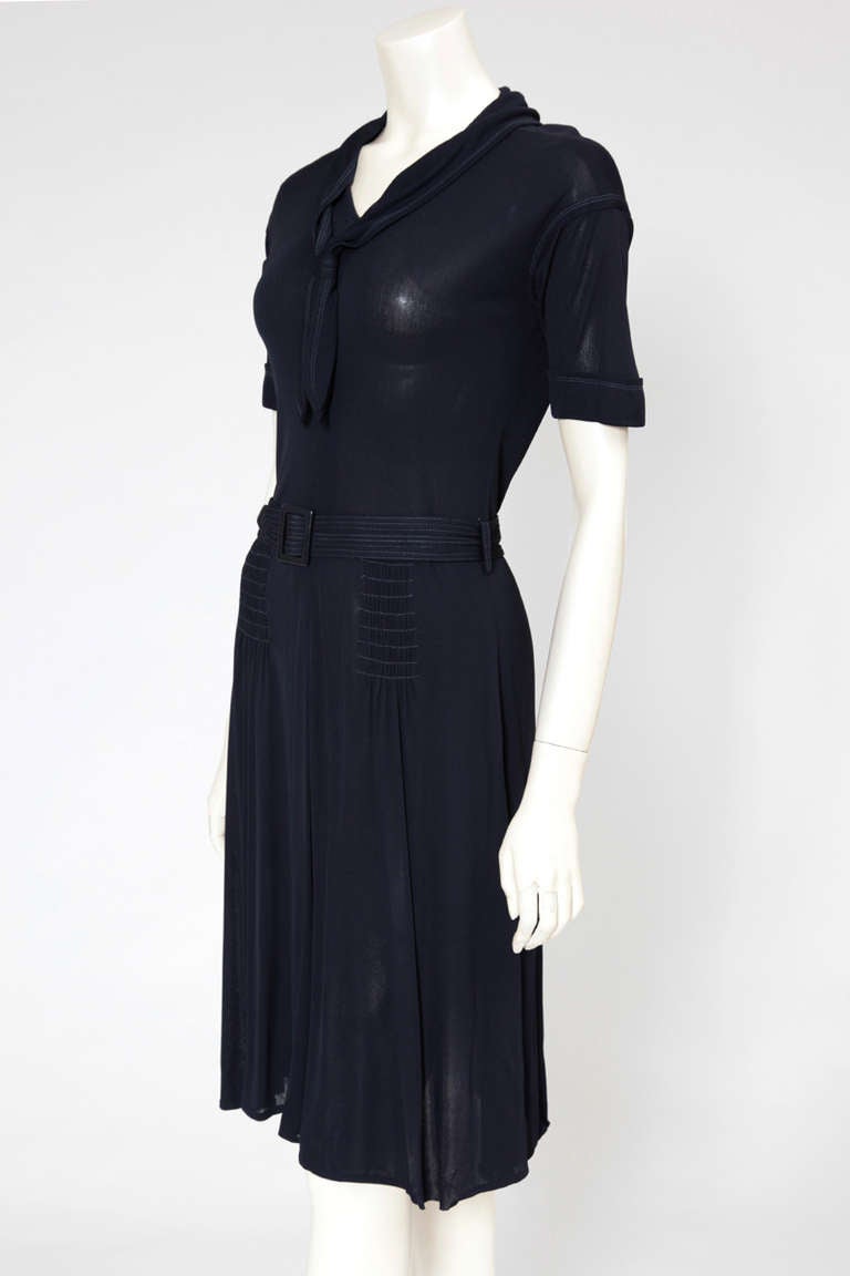 70’s Jean Muir navy fine jersey dress with short sleeves and sailor collar on front and back. Matching belt, smocks at both hips, stitching effects, two side pockets and zip in the back. This piece has a multitude of refined details who turn a