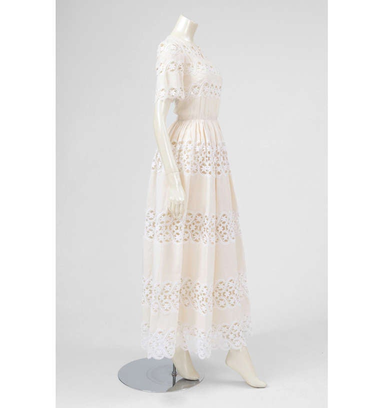 A ravishing and romantic piece of Valentino haute couture dating from the 70's. The short sleeved see-through guipure and cotton dress features a cut-out detail at the neckline. Fitted bodice and gathered waist line create a fuller skirt flaring out