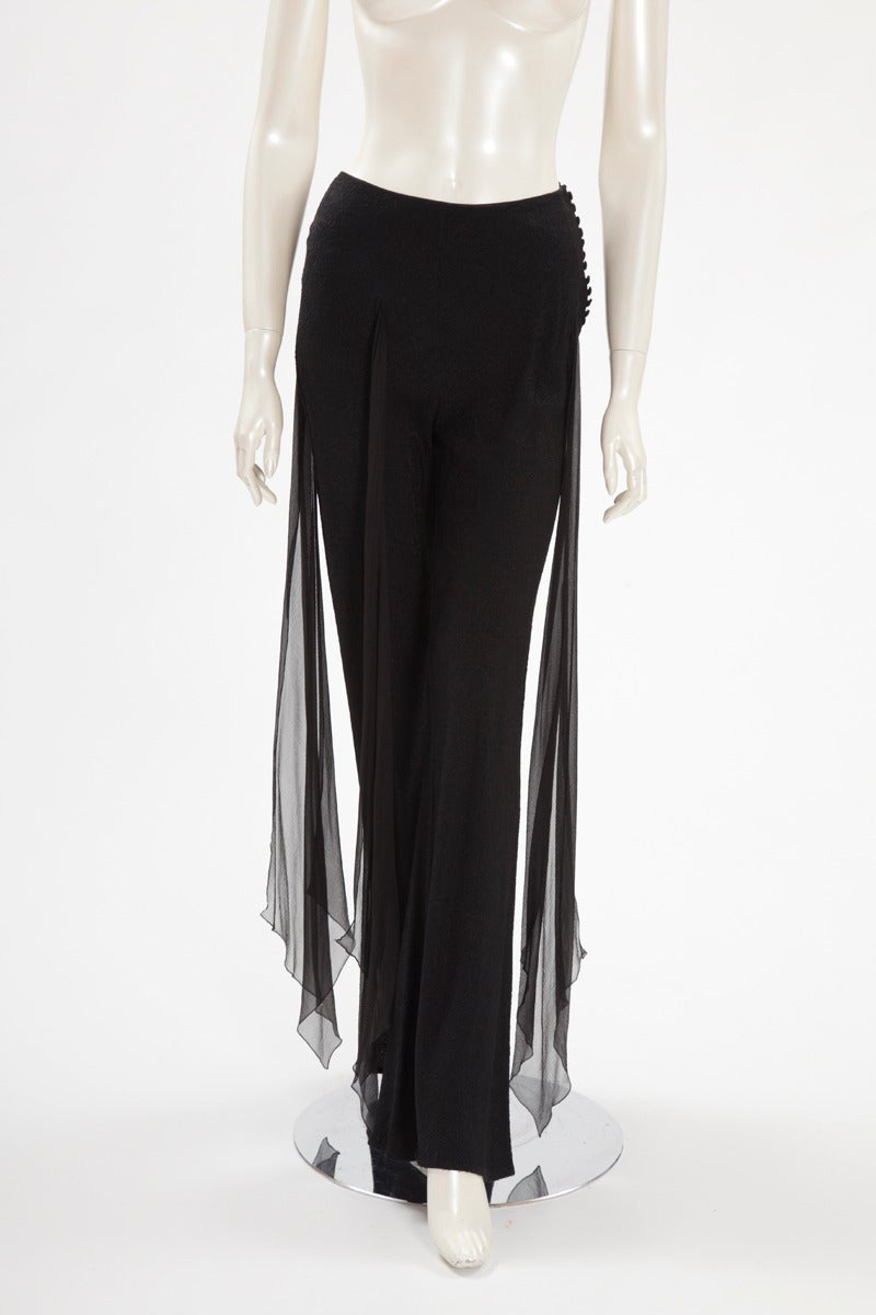 Unusual John Galliano black silk pants. Flowing shape. Four long sections of black silk chiffon get out from the textured silk. Side closure on the left with a row of covered buttons.

Fits approx. : US 2-6 / FR 36-38 

Measurements :
Waist