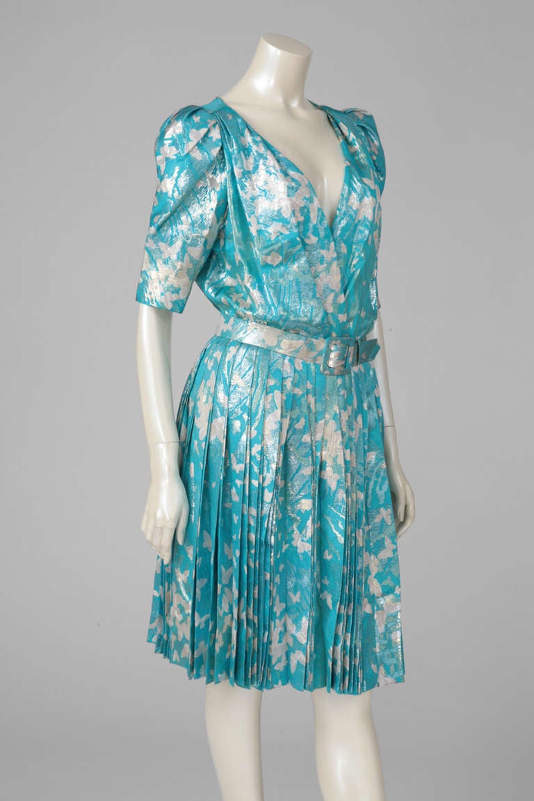 Elegant early 80's haute couture “patron original” turquoise printed cocktail dress with heavily pleated skirt. Wrapped bodice. Hourglass nipped-waist. The structural pleating gives the garment depth and texture. The print features white lurex