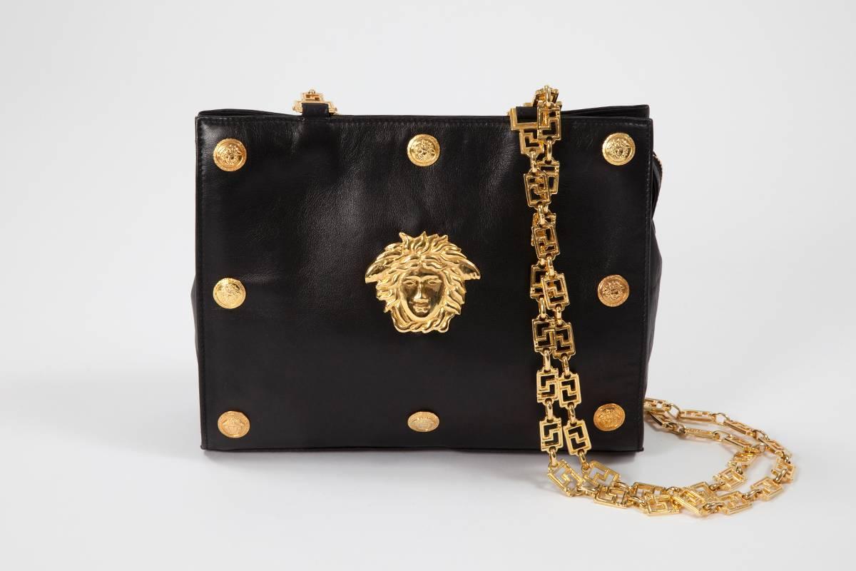 Glamorous Gianni Versace Couture shoulder bag with iconic gold Medusa medallions at the front. The metal shoulder straps are made of the famous Versace signature logos. Crafted in soft black leather, the bag is lined with black leather featuring a
