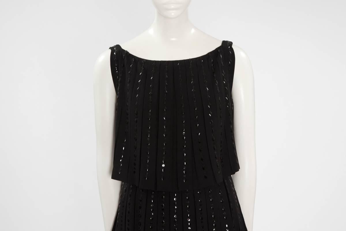 Robe de cocktail en laine noire perlée de Norman Hartnell, fin des années 60, composée de trois étages plissés tombant en une gracieuse cascade. Embellie de magnifiques paillettes noires rondes et en forme de diamant, la robe se ferme par une