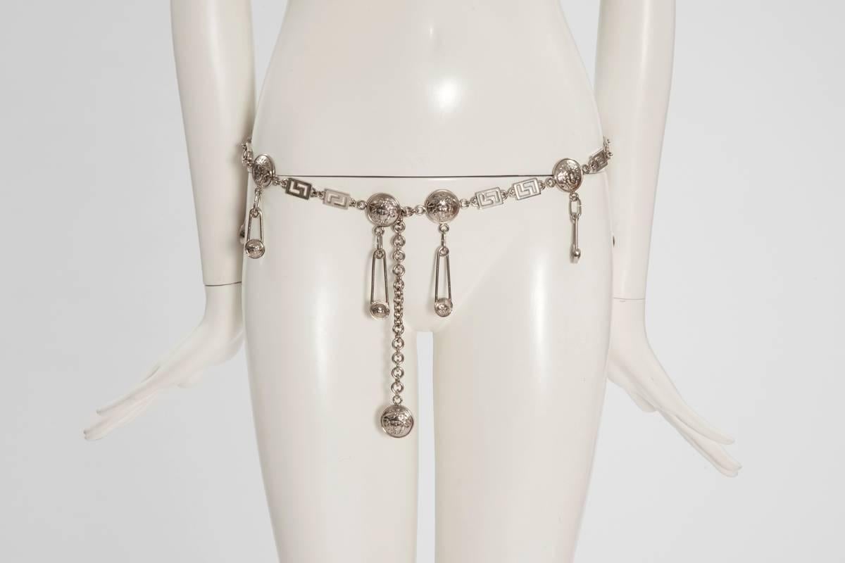 Important 90’s Gianni Versace link chain belt, playfully adorned with dangling safety pins medallions / charms. The various size safety pins have the iconic Medusa imprint. This weighty style belt is crafted from silver-tone metal and has an