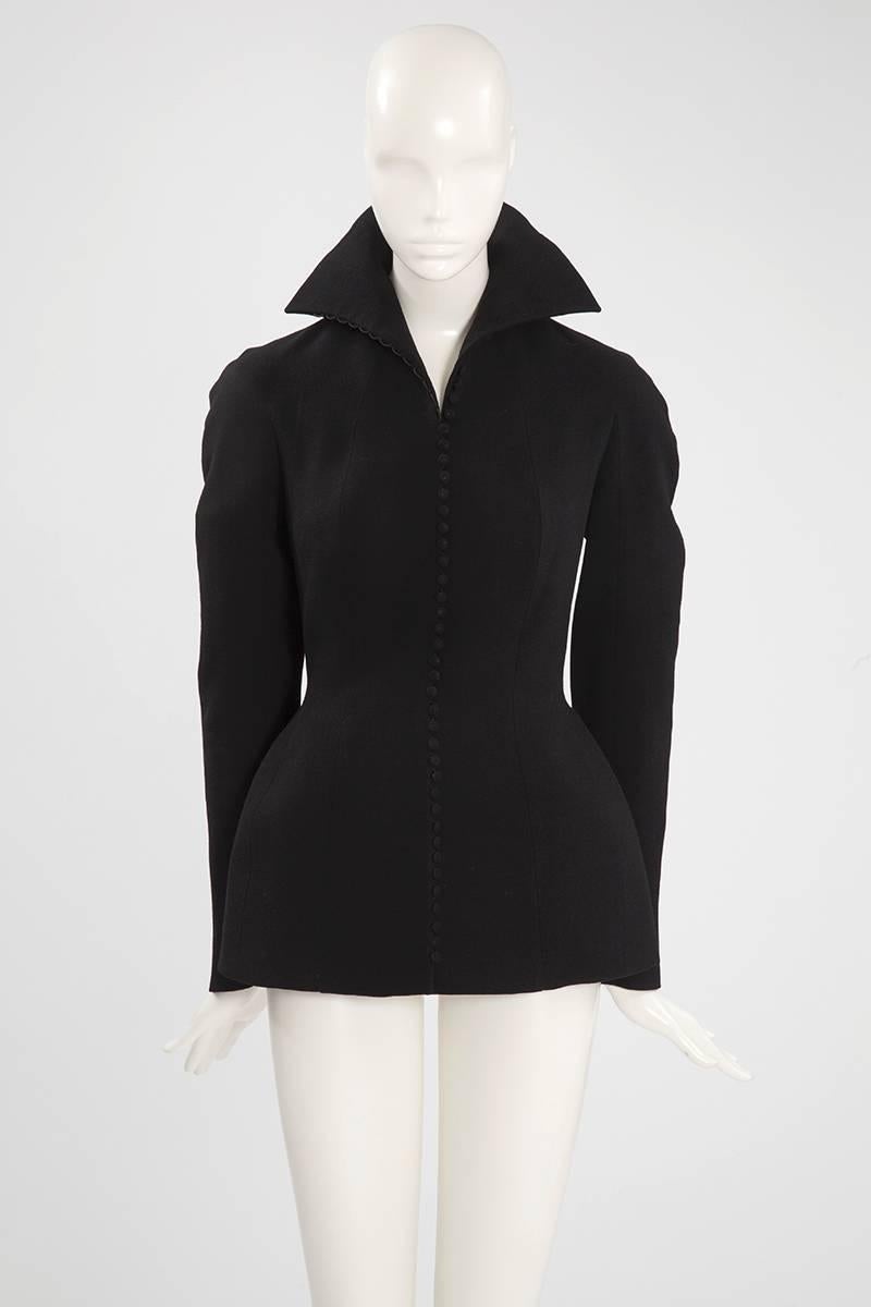 This fantastic John Galliano blazer jacket is tailored in structured black wool. Gently curved at the shoulders (raglan cut), this slim-fit style nips in at waist and flares out into a flattering peplum. It closes with 46 little covered buttons down