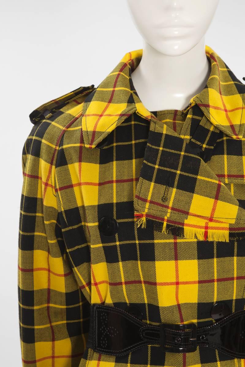 With this bold tartan, Jean Paul Gaultier reinterprets the classical trench coat. This never worn piece is tailored from a yellow wool tartan fabric with waterproof backing and finished with a black elasticized patent leather belt. The trapeze shape