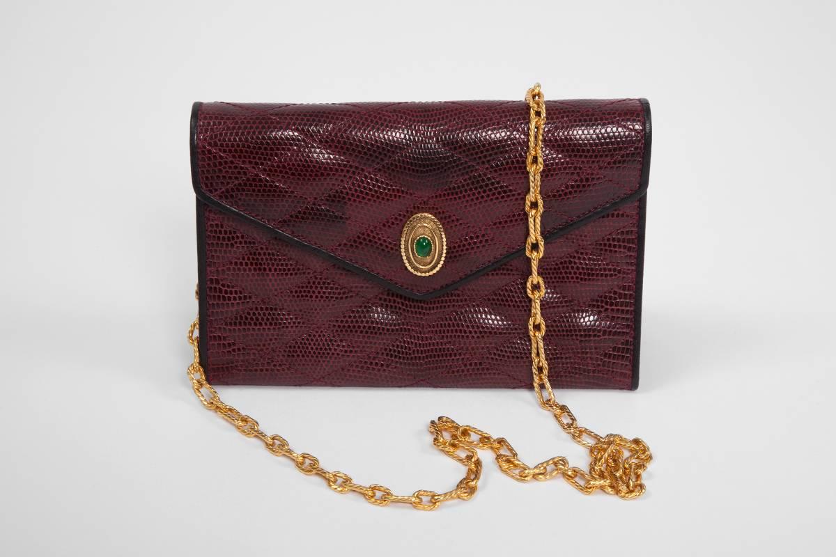 Unusual vintage Chanel bag in garnet red lizard skin and black leather piping, embellished with an elegant green Gripoix glass medallion adorning the flap. Its single strap is crafted in a textured gold link chain. Snap closure. Matching garnet red