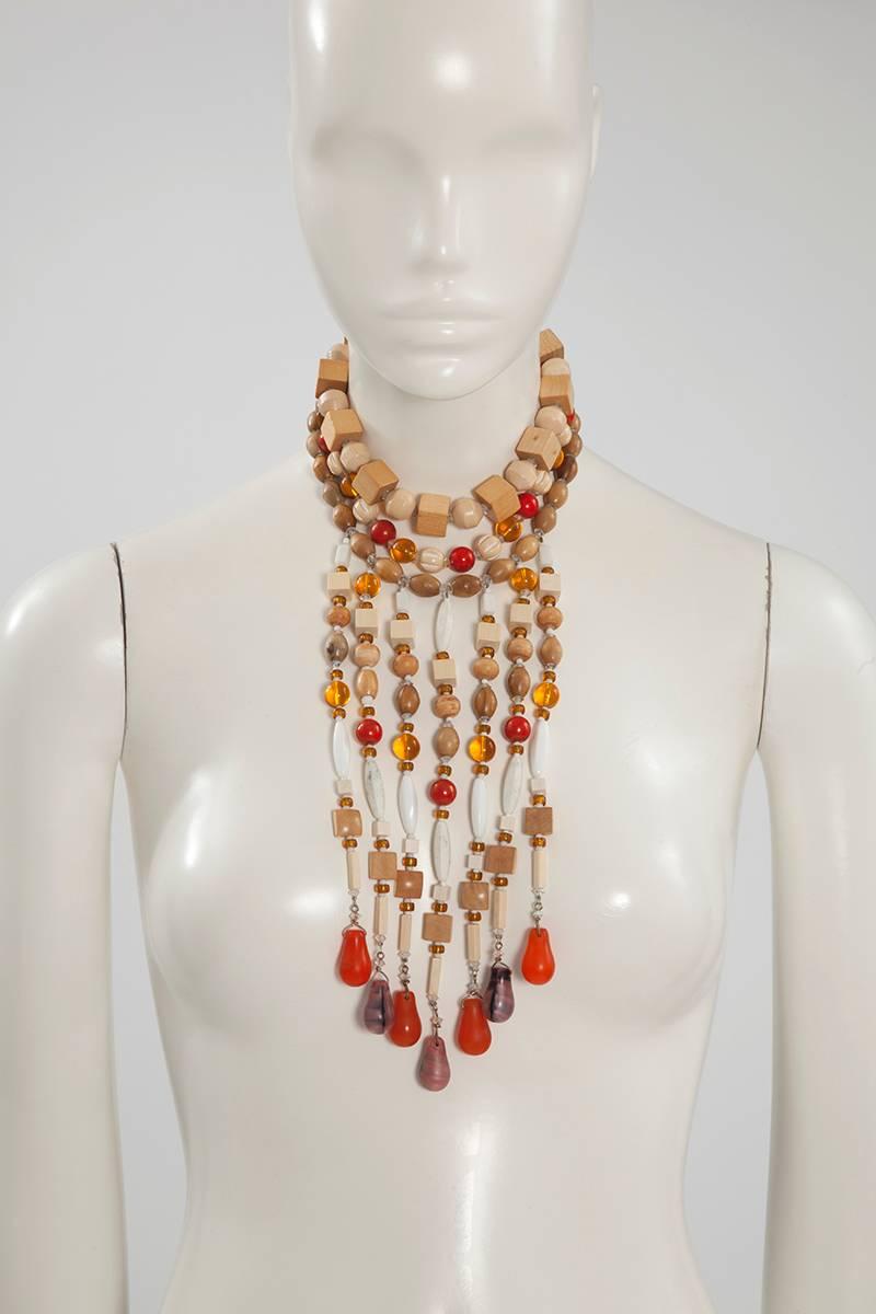 Très rare collier multibrins insolite rappelant certains motifs des robes de la collection africaine haute couture YSL 1967. Façonnée avec du bois, diverses pierres (jaspe rouge et marbre blanc), du verre, du verre fondu et des strass de différentes