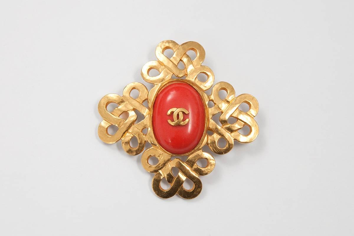 A Chanel brooch can transform the simplest outfit into really something ! This 1997 Spring-Summer exemplar is crafted from an intricate gilt metal arabesque highlighting a faux red coral in its center, adorned with the Chanel logo. The brooch is