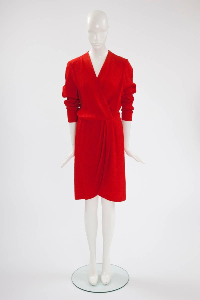 This early 90's YSL cocktail dress is an elegant and chic option for any special occasion. Crafted in tactile blistered silk in a striking orange-red hue, the dress features a flattering V-neckline. This wrap-style piece gathers at the waist with a