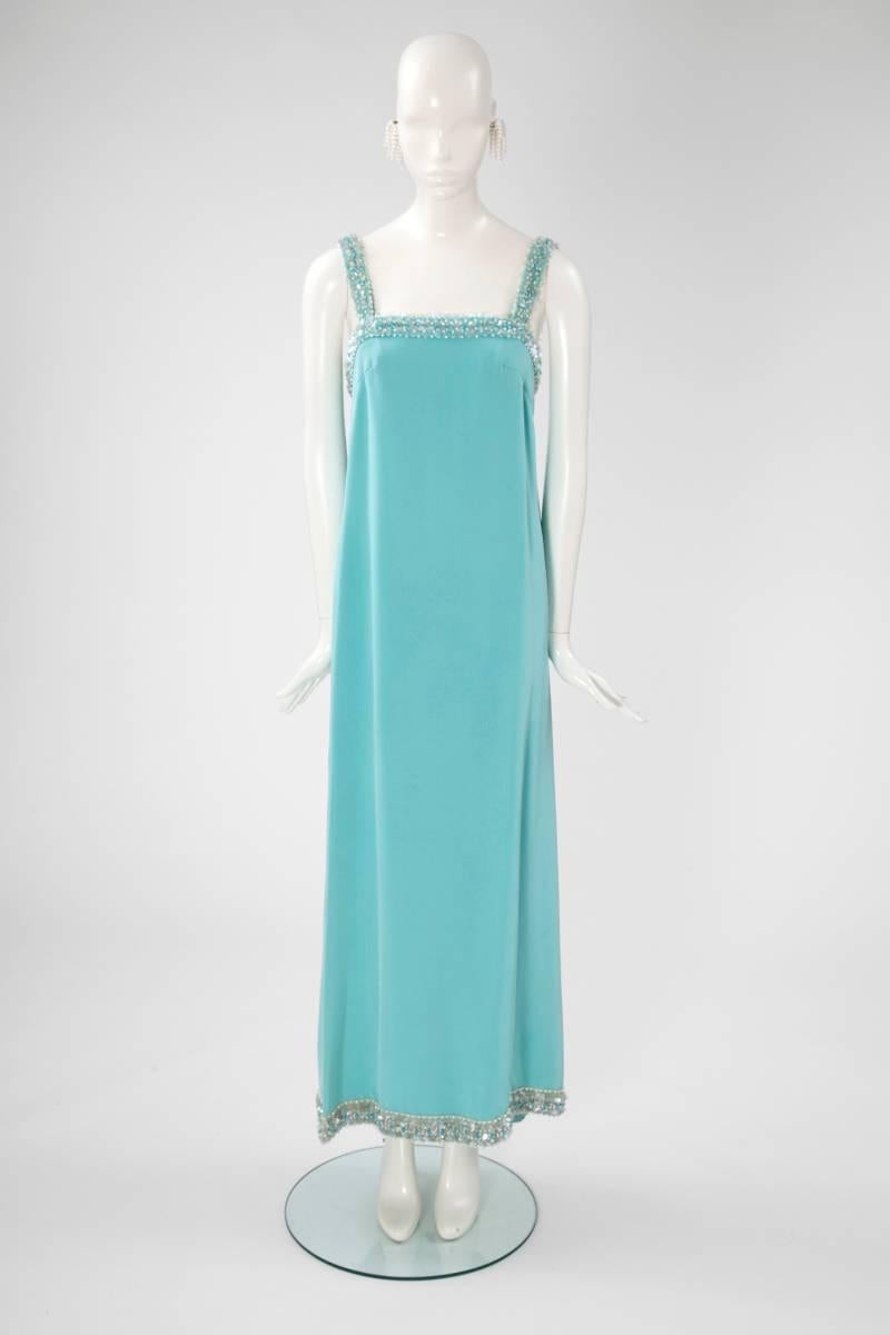 Exquisitely well made, this wonderfully chic unknown 60’s turquoise silk crepe gown, with its cute back train, will be perfect for any party or event. The gown is beaded over the bust and around the hemline and is offered with an original pair of