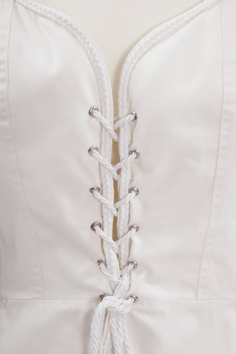 From the iconic 1977 YSL Spring-Summer ready-to-wear collection, this white cotton corset top is a major essential to complete any refined modern wardrobe. Puffed sleeves, laced up corset, white braid trim edging, belt-sash with silk fringed tassel