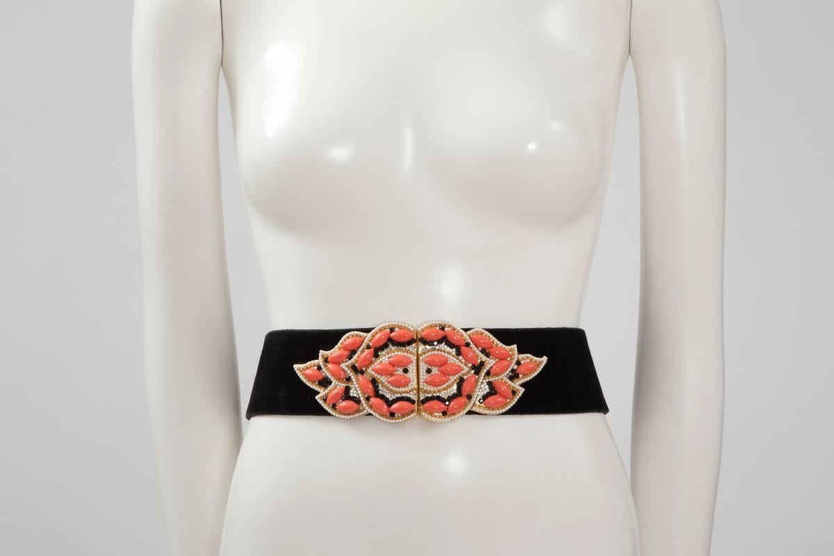 From a still active luxury boutique in Vienna, Autria, spectacular 70's « Henryks Bijoux » black velvet and leather belt with large golden metal faux pink coral and strass jewels buckle. The belt closes with a hidden large hook and eye. The width of