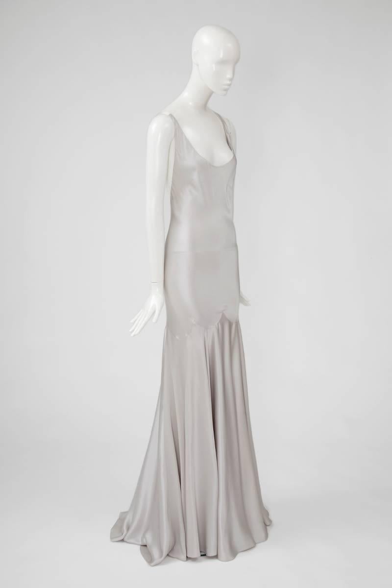 Incredibly sexy tough elegant, this gown by the enfant terrible of British fashion, Alexander McQueen, is crafted from lustrous light grey silk-charmeuse, skimming the body and falling into a dramatic godet pleats puddle train. Featuring a plunging