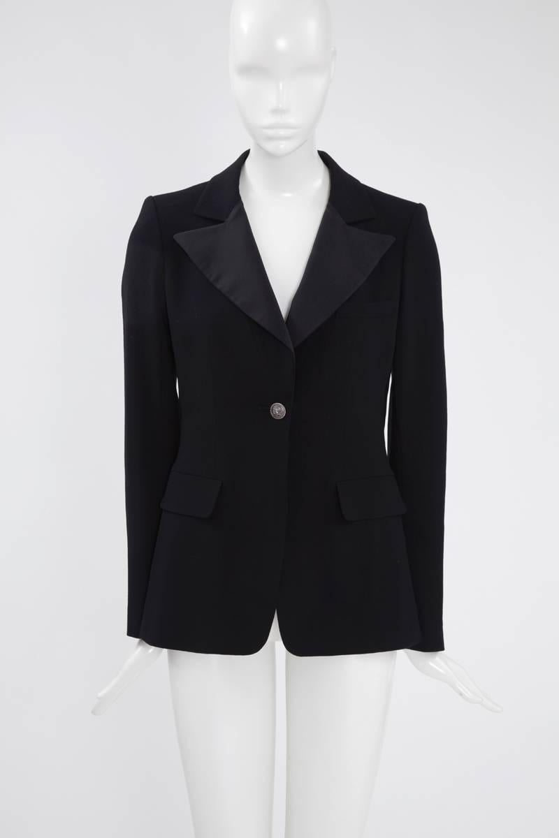 Tailored as softly nipped-in waist, this Chanel black wool blazer has a collar, which is partly trimmed with matte satin lapels. It closes with one lion head metal button and features two flap pockets. Fully lined in refined black silk, it is a