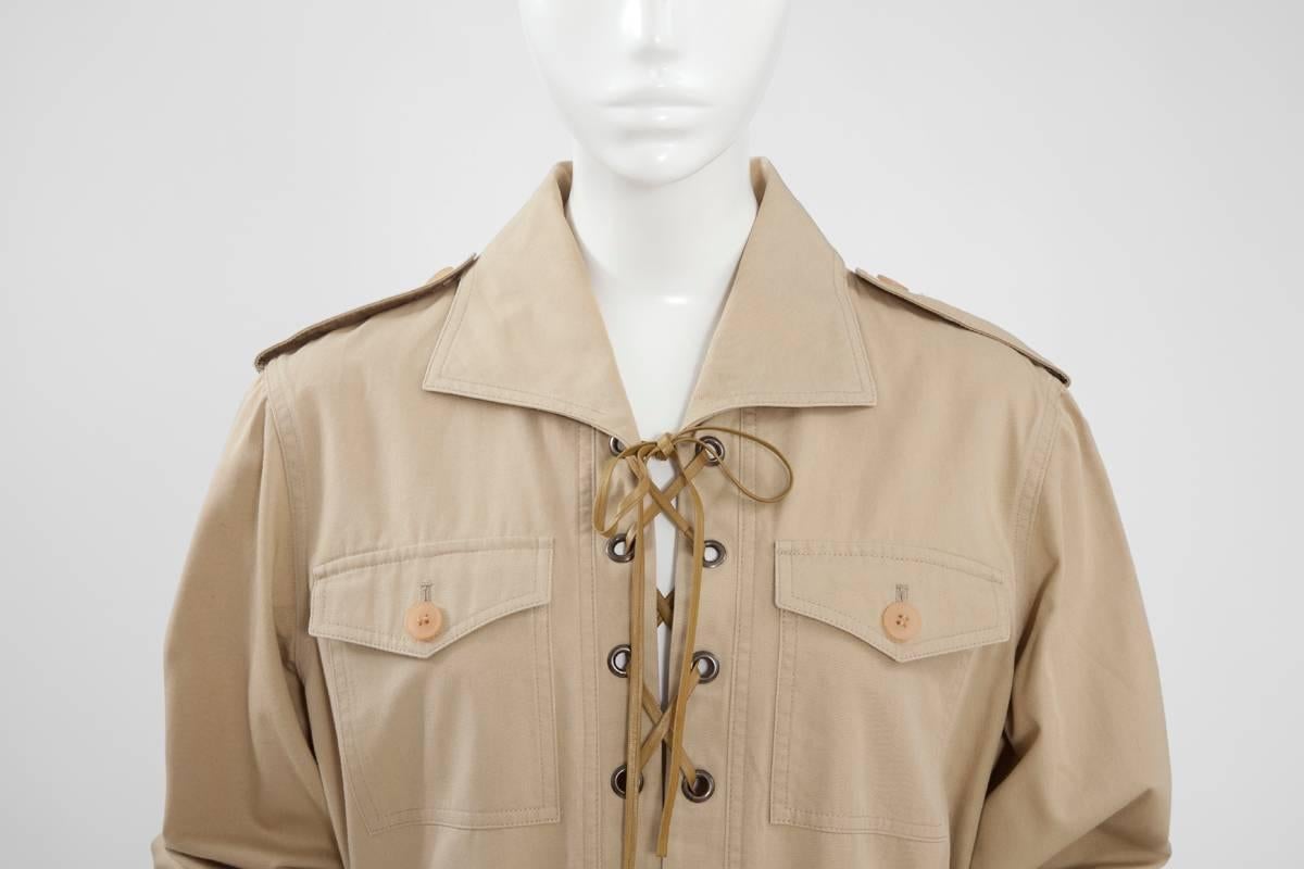 A fantastic version of the iconic “saharienne” first debuted in 1968. This vintage lace up safari tunic top is constructed in tan-beige cotton canvas and leather string. Long sleeved, with a matching belt with metal buckle, it features four bellow