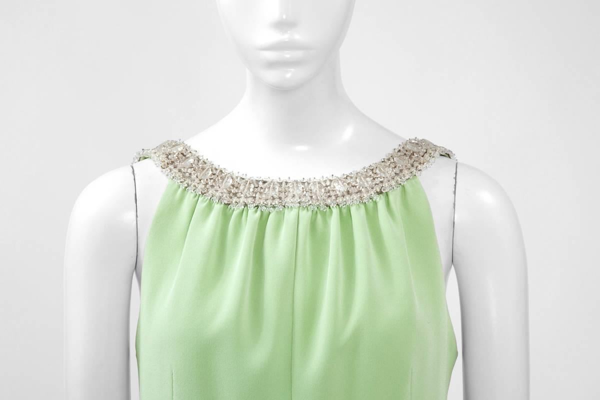 A wonderful chic cocktail option, this unlabelled haute couture dress is made of a refined shade of pastel green silk crepe. The flattering 60’s shift silhouette is enhanced with a band of light silver lurex along the neckline, the back and the
