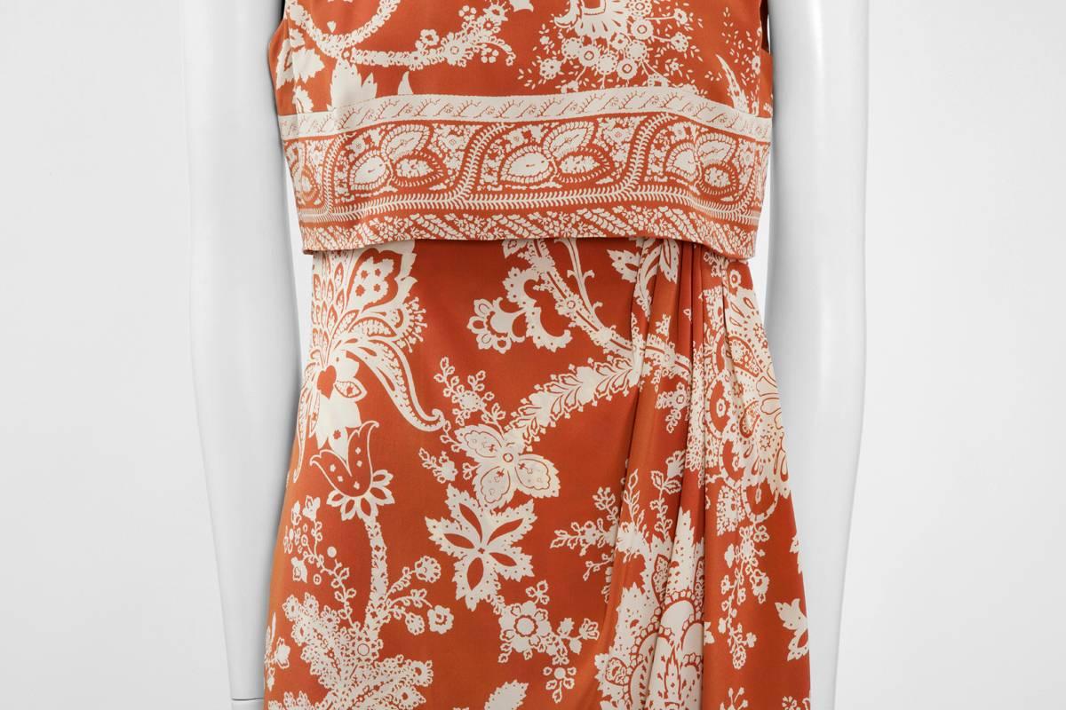 Constructed in rust silk with an ivory paisley pattern, this early 90’s Valentino dress is draped on the left side and features a high neckline. Giving a two pieces illusion, it fastens in two steps : the dress is zipped at first along the back,