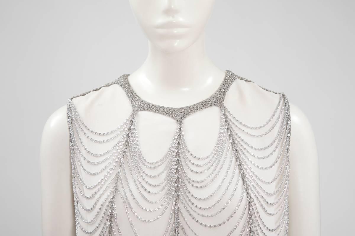 The spirit of the 20's in a 70's Loris Azzaro dress ! Constructed in a white crepe, this unlabeled Azzaro sleeveless shift dress has a slight A-line silhouette. Embellished with silver lurex mesh and chains which form a pattern of superseding mobile