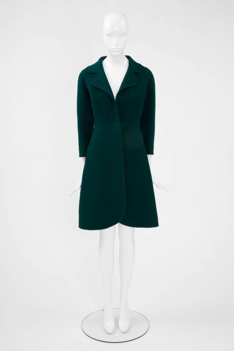 Constructed in a refined deep bottle green wool, this Miguel Rueda haute couture coat features a double lapel collar and ¾ sleeves. Unlined, it fastens in the front with one hidden button (see picture 3). No pockets. Expertly cut, the coat enhances