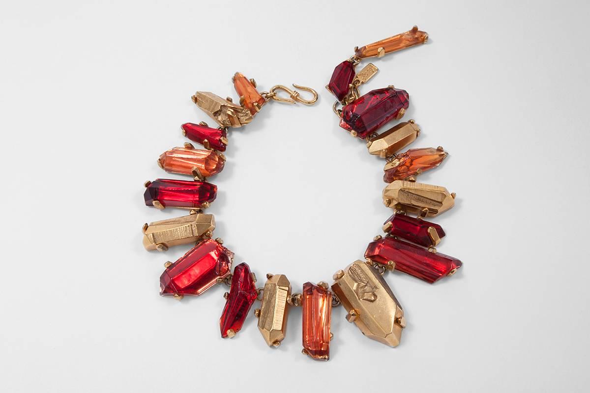 This gilt metal Yves Saint Laurent chunky necklace features irregular faux red quartz resin crystals set in ostensible faux gold claws. Hook and eye closure at the back. The length of the necklace is adjustable and features the “YSL” logo tag (see