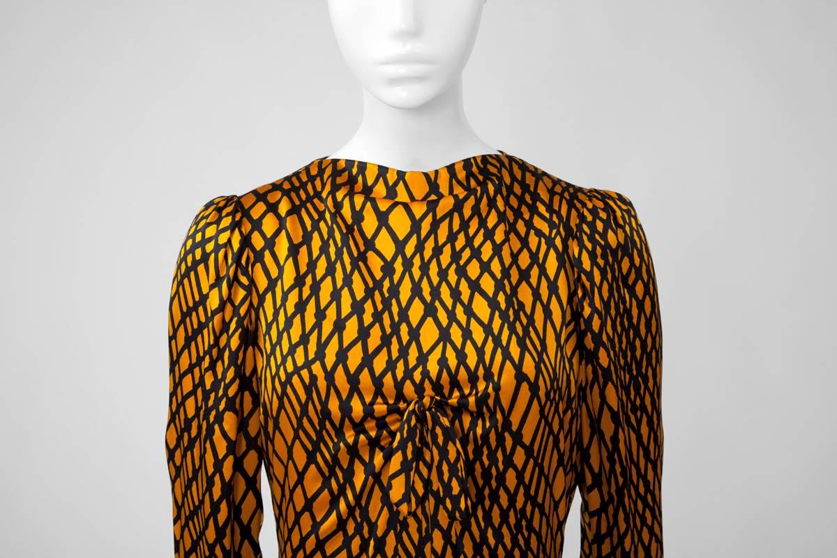 Une belle et rare trouvaille de haute couture, cette robe du soir YSL des années 70 est faite de satin de soie raffiné, présentant un motif noir abstrait sur un riche fond de citrouille dorée. En épousant délicatement le corps, il offre une
