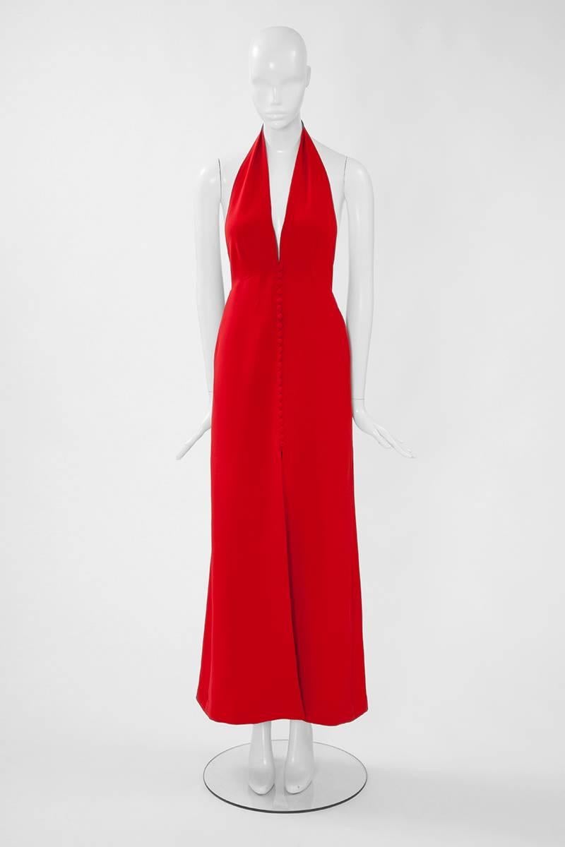 A 70’s bright red silk crepe evening dress from the “forgotten” Italian fashion house Alma Calzoni. This dress features a deep V-neckline and 23 fabric covered buttons fastening to the front. With its halterneck design, this dress is incredibly