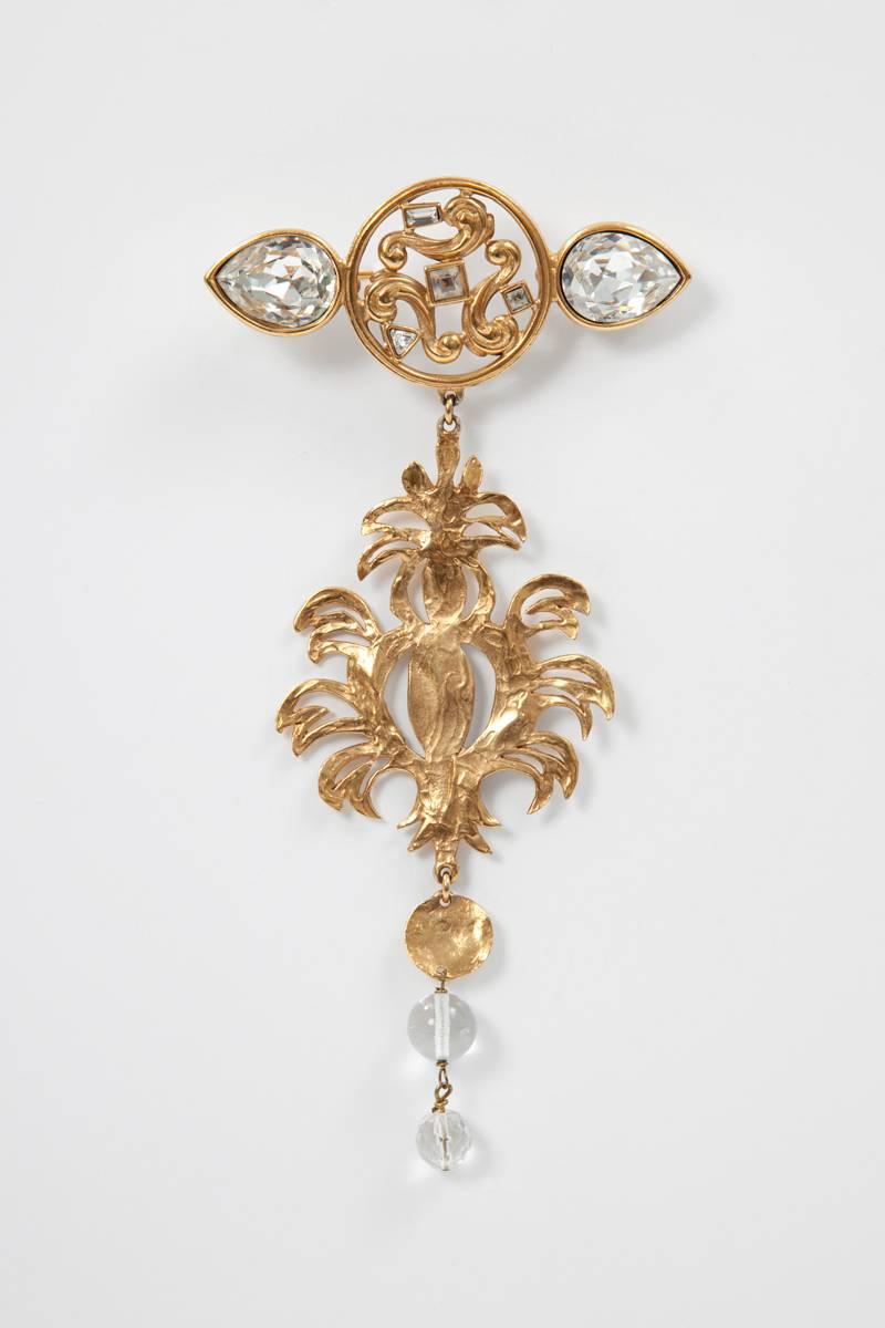 Rare gilt “palm tree/figurine” YSL brooch decked with geometric faceted glass. The palm tree/figurine is in hammered gilt metal. Two crystal glass teardrops ornate the lower part. The brooch is signed 