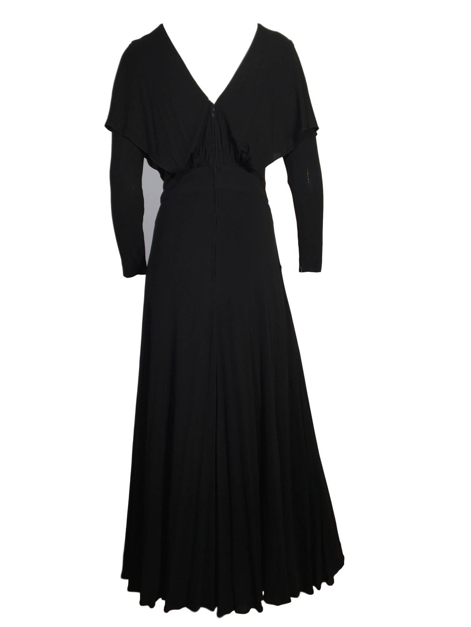 Black silk jersey full length evening dress, from the 1960s/70s era, with long fitted sleeves that fasten with a zip, gathered feature and layered detail on bodice and long sweeping skirt, fastens at the back with a zip and is lined with a satin
