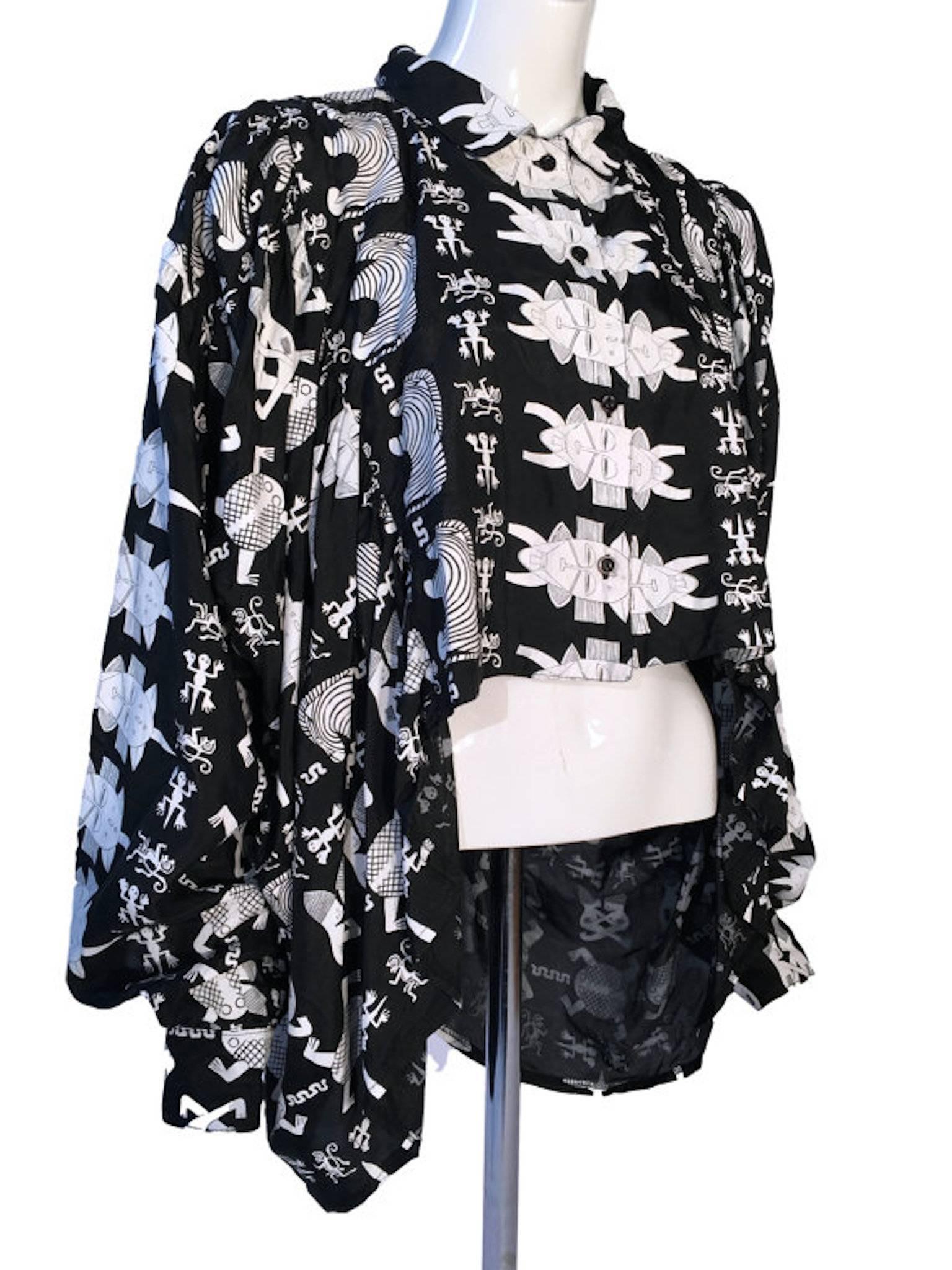 A rare Barbara De Vries Giraf black & white 100% silk cropped front batwing blouse. With tiki print, button front fastening. Fabulous cut with a manteau cape style effect. Sleeves have flitted buttoned cuffs.

Size UK 8/10, 14 inches across