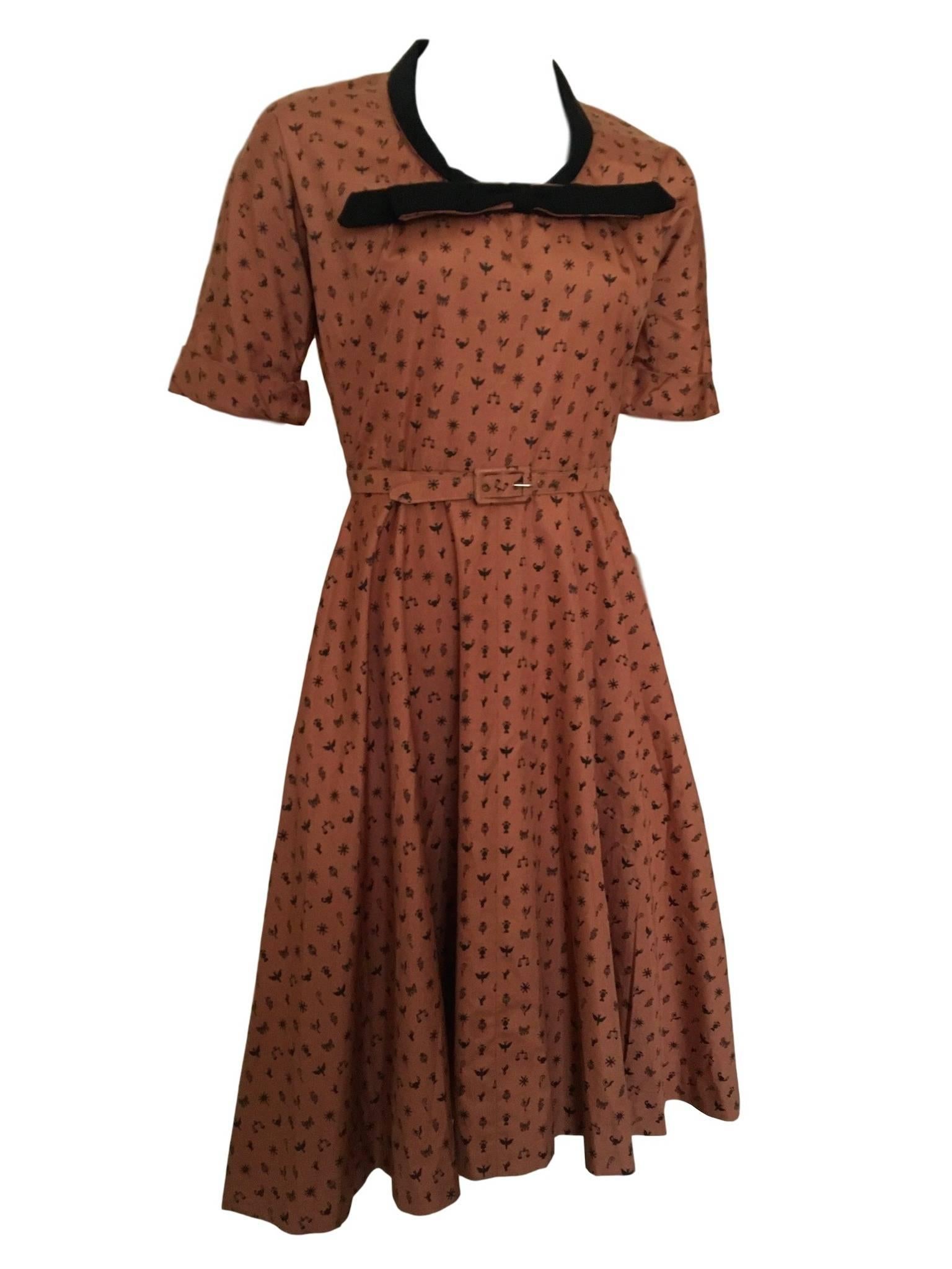 Horrockses cotton vintage 1950s dress, with novelty print of zodiac and other images. A deep orange/bronze colour with black print, a scooped neck line with bow feature, fitted waist band, flared skirt and has original belt.

Size 8/10 measures 18
