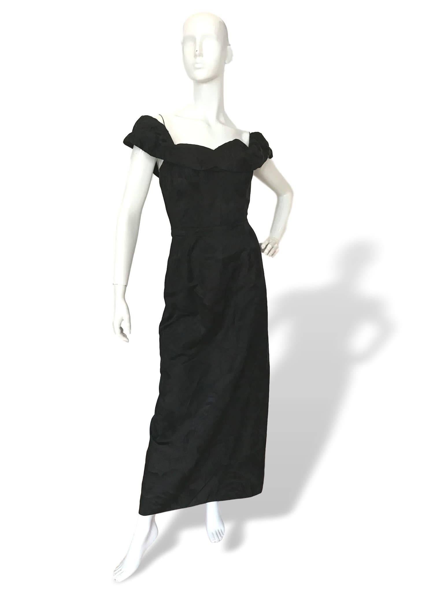 A black 1950s unlabelled couture standard black evening dress, in floral and leaf satin damask material, shelf bust, boned bodice with off shoulder feature, made up of 2 pieces, main dress is fitted and outer piece fitted onto waist line giving a