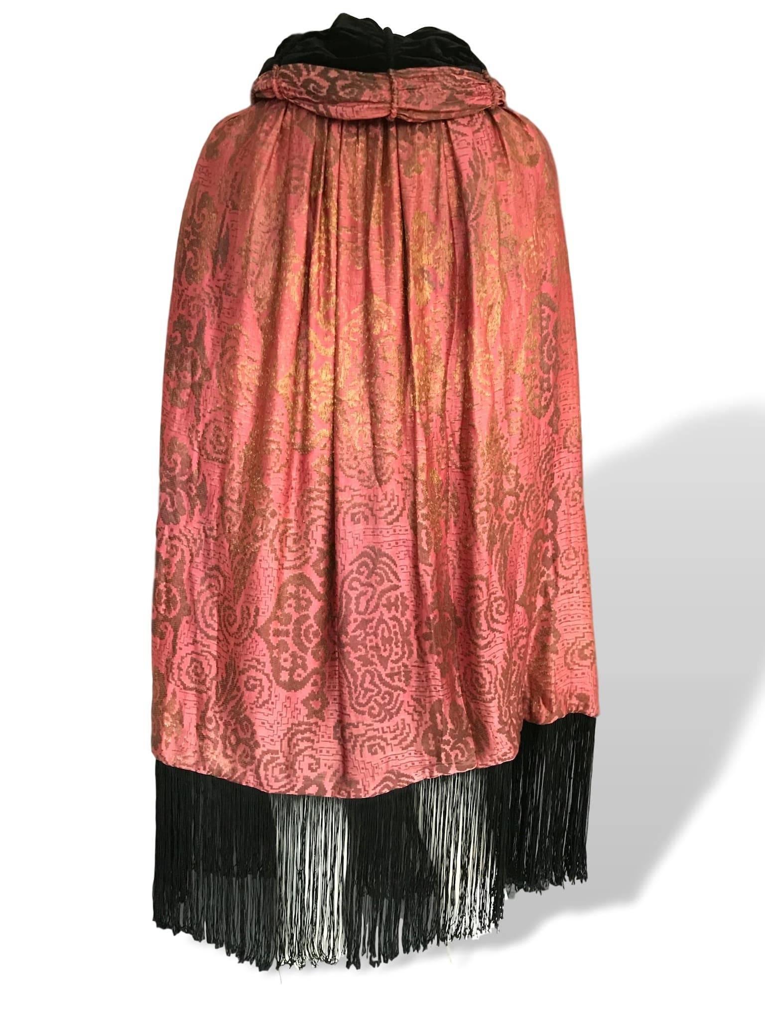 1920s reversible gold metallic damask pink silk and black velvet on reverse cocoon coat/cape. With fringed hem and button neck fastening on both sides. 
In very good condition, a small section of fringe is missing on the hem. Measures 50 inches in