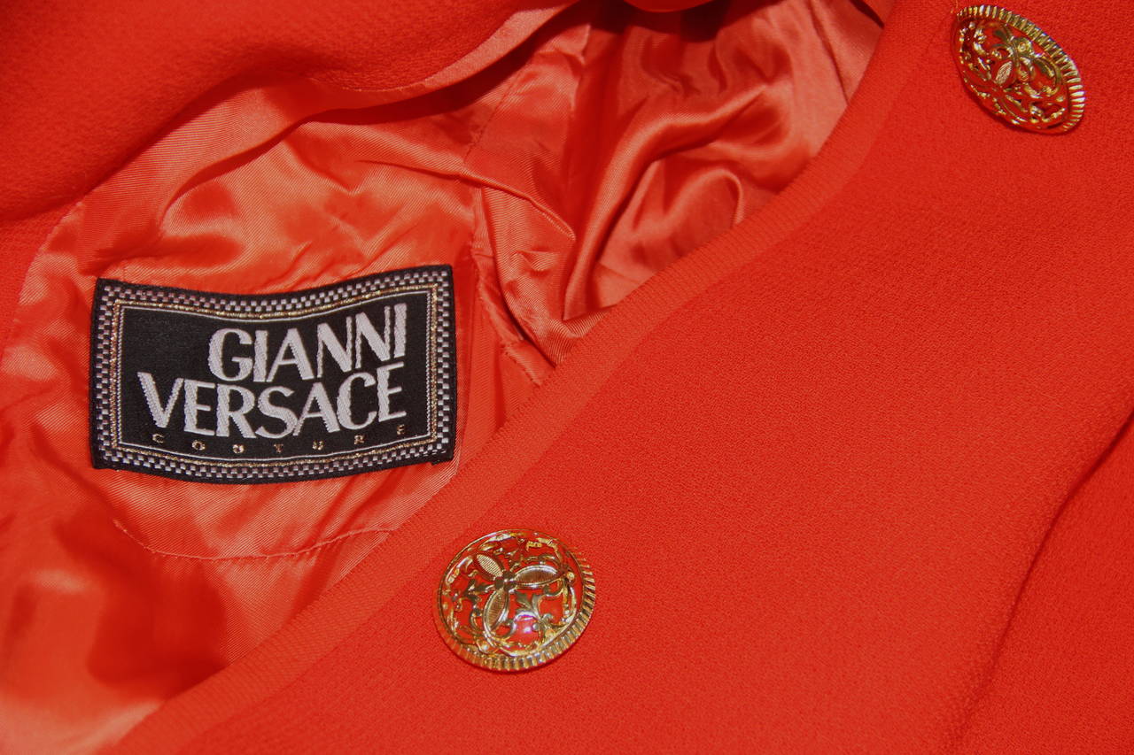 Gianni Versace orange dress coat from the Fall 1991 collection.

The coat is secured at the front and the cuffs by a series of oversized gold-tone metal and glass buttons.

Marked an Italian size 40.

Manufacturer - Alias S.p.a.

Fabric