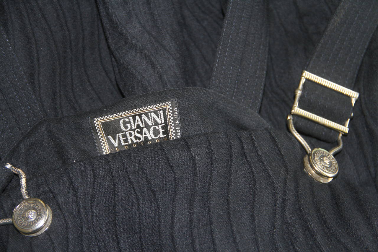 Gianni Versace black wool textured pinafore romper from the Fall 1994 collection. The romper is secured by silver-tone metal Medusa embossed harness clips.

Marked an Italian size 40.

Manufacturer - Alias S.p.a.

Fabric content - 90% wool /