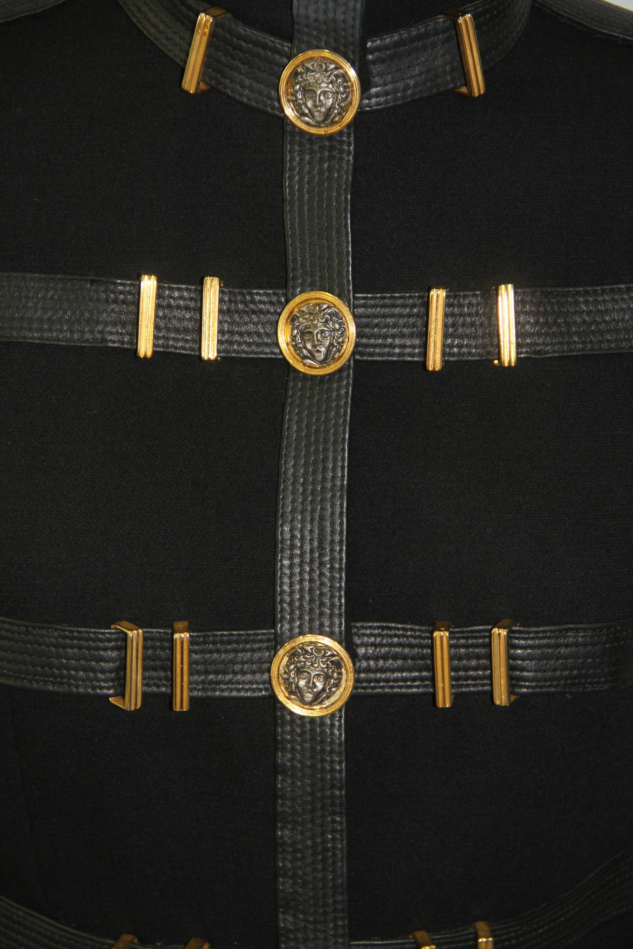 Museum quality Gianni Versace black wool suit from the Fall 1992 Bondage collection.

The suit features black leather bondage straps to the jacket and skirt, together with oversized gold-tone and silver tone Medusa embossed discs and buckles. The